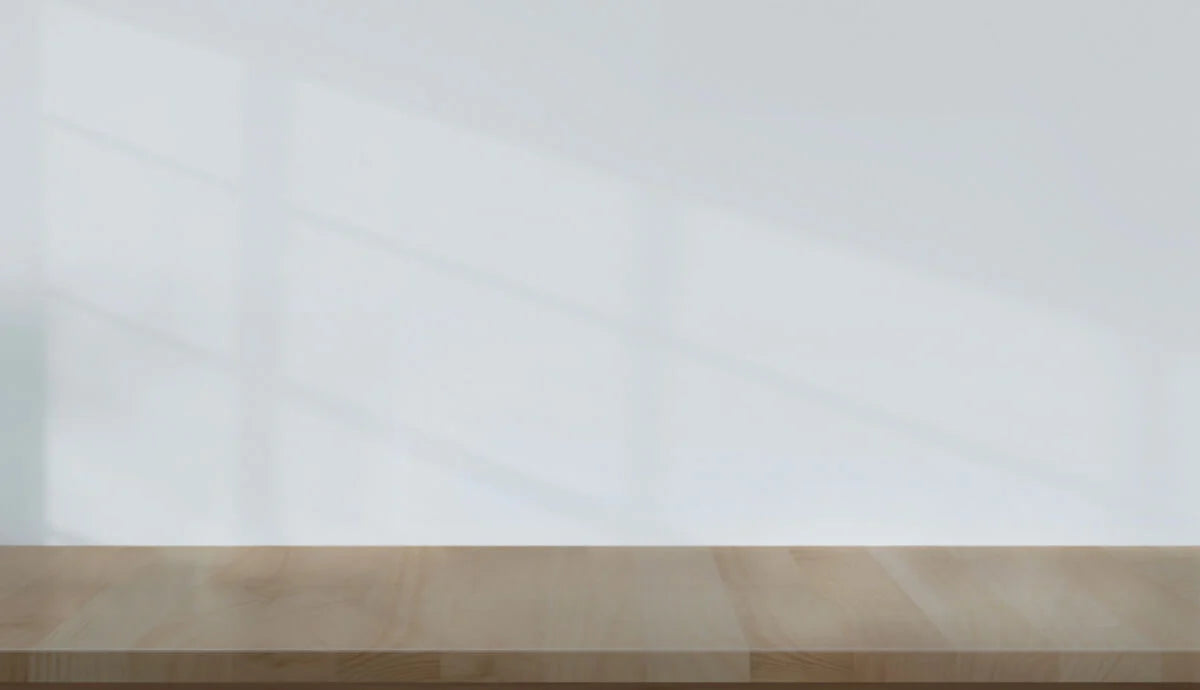 A light, neutral-colored wall with a wooden surface below it. The wall features soft shadows, likely from a window, creating a subtle texture. The wooden surface appears smooth with a natural grain pattern. Overall, the image conveys a calm, minimalist aesthetic with a focus on simplicity.