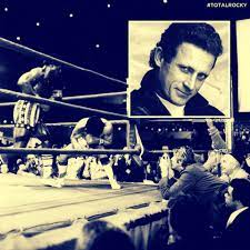 A black and white image of a boxing scene, featuring two fighters in the ring, one is throwing a punch while the other appears to be bending forward. In the background, a crowd is visible, some people are cheering or reacting. There is a smaller inset image in the upper corner, showing a close-up of a man with short dark hair and a thoughtful expression. The overall atmosphere conveys the intensity of a boxing match combined with the focus on the inset portrait.